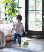 Toddler walking indoors pulling the Plan Toys Dancing Alligator wooden pull along toy across a wood floor