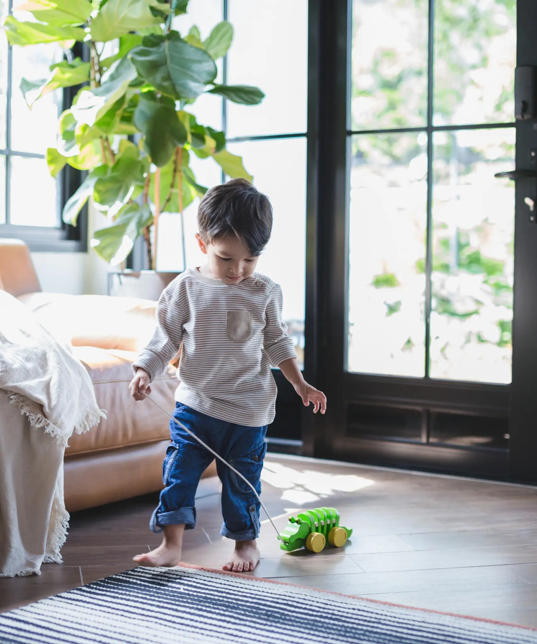 Toddler walking indoors pulling the Plan Toys Dancing Alligator wooden pull along toy across a wood floor