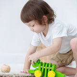 Toddler kneeling down to reach for the Plan Toys Dancing Alligator wooden pull along toy
