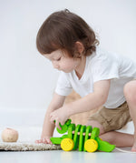 Toddler kneeling down to reach for the Plan Toys Dancing Alligator wooden pull along toy