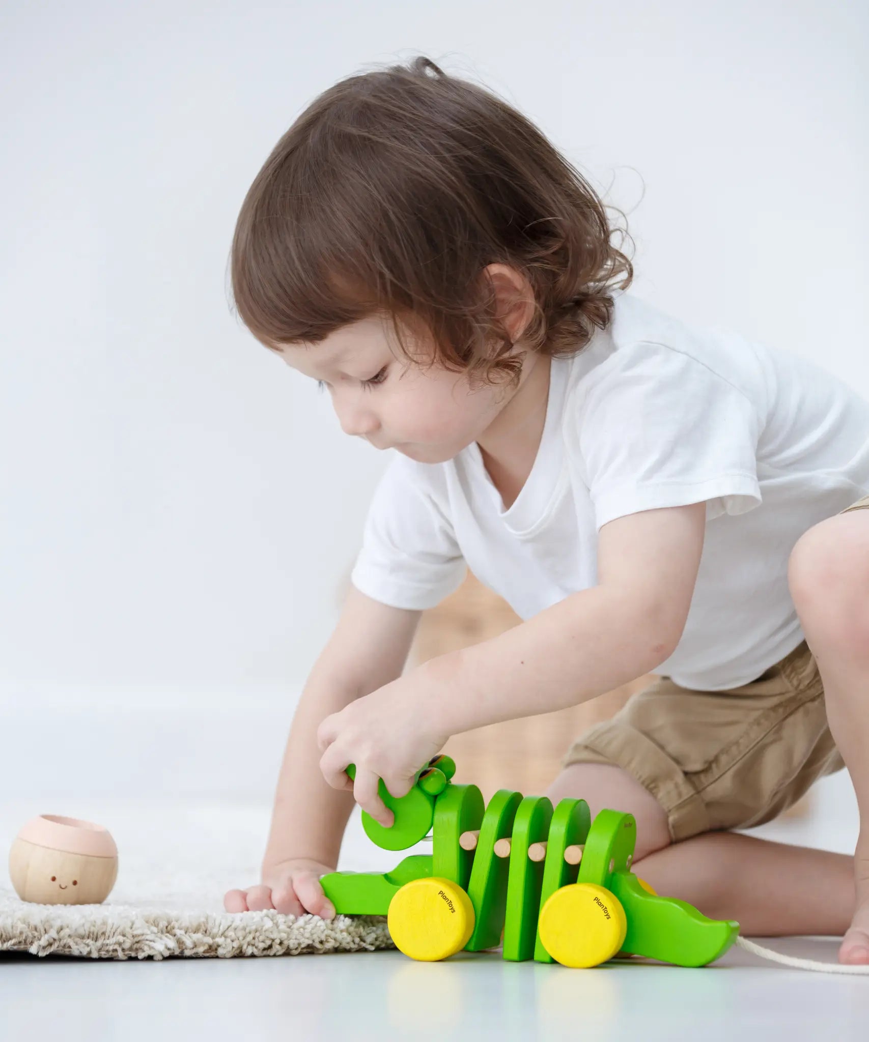 Toddler kneeling down to reach for the Plan Toys Dancing Alligator wooden pull along toy
