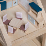 The pieces from the PlanToys Dining Room Dolls House Furniture set placed in a room in a wooden dolls house. 
