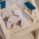 The pieces from the PlanToys Dining Room Dolls House Furniture set placed in a room in a wooden dolls house. 
