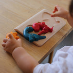 A close up of a child playing with the PlanToys Dino Puzzle on a wooden table. 