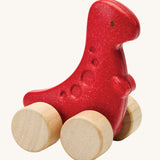 PlanToys dino rex wooden car toy. A red coloured, wooden tyrannosaurus rex dinosaur figure toy on wheels. PlanToys range of toys are made from sustainably sourced rubberwood, we're proud stockists of PlanToys here at Babipur. 