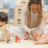 Two children and an adult playing with the PlanToys Dino wooden Car toys. A blue coloured diplodocus, a yellow stegosaurus and red coloured t-rex dinosaur figures on wheels. PlanToys range of toys are made from sustainably sourced rubberwood, we're proud stockists of PlanToys here at Babipur. 