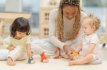 Two children and an adult playing with the PlanToys Dino wooden Car toys. A blue coloured diplodocus, a yellow stegosaurus and red coloured t-rex dinosaur figures on wheels. PlanToys range of toys are made from sustainably sourced rubberwood, we're proud stockists of PlanToys here at Babipur. 