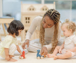 Two children and an adult playing with the PlanToys Dino wooden Car toys. A blue coloured diplodocus, a yellow stegosaurus and red coloured t-rex dinosaur figures on wheels. PlanToys range of toys are made from sustainably sourced rubberwood, we're proud stockists of PlanToys here at Babipur. 