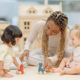 Two children and an adult playing with the PlanToys Dino wooden Car toys. A blue coloured diplodocus, a yellow stegosaurus and red coloured t-rex dinosaur figures on wheels. PlanToys range of toys are made from sustainably sourced rubberwood, we're proud stockists of PlanToys here at Babipur. 