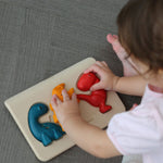 An overhead view of a child playing with the PlanToys Dino Puzzle, They have their hands on the orange and red dinosaur pieces. 