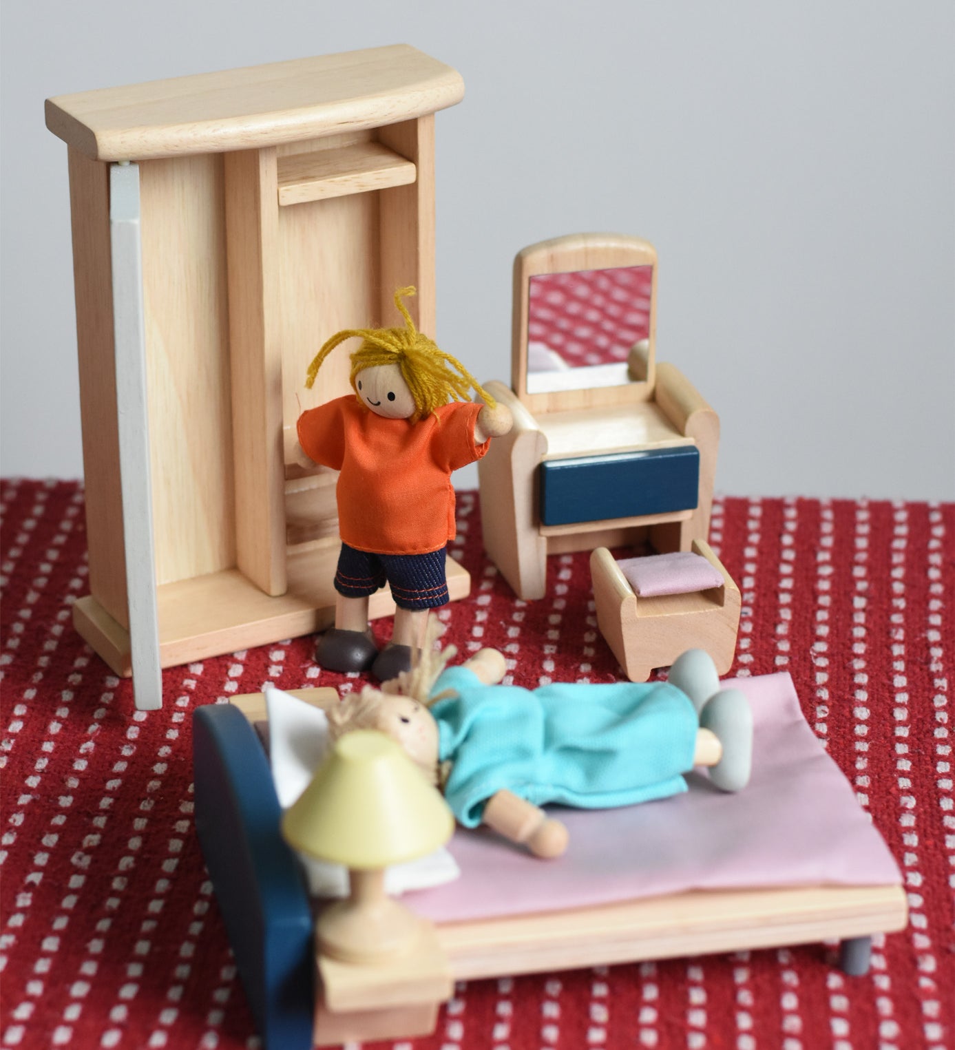 Two PlanToys peg dolls positioned in an imaginative play scene, with the orchard dollhouse wooden bedroom furniture. 