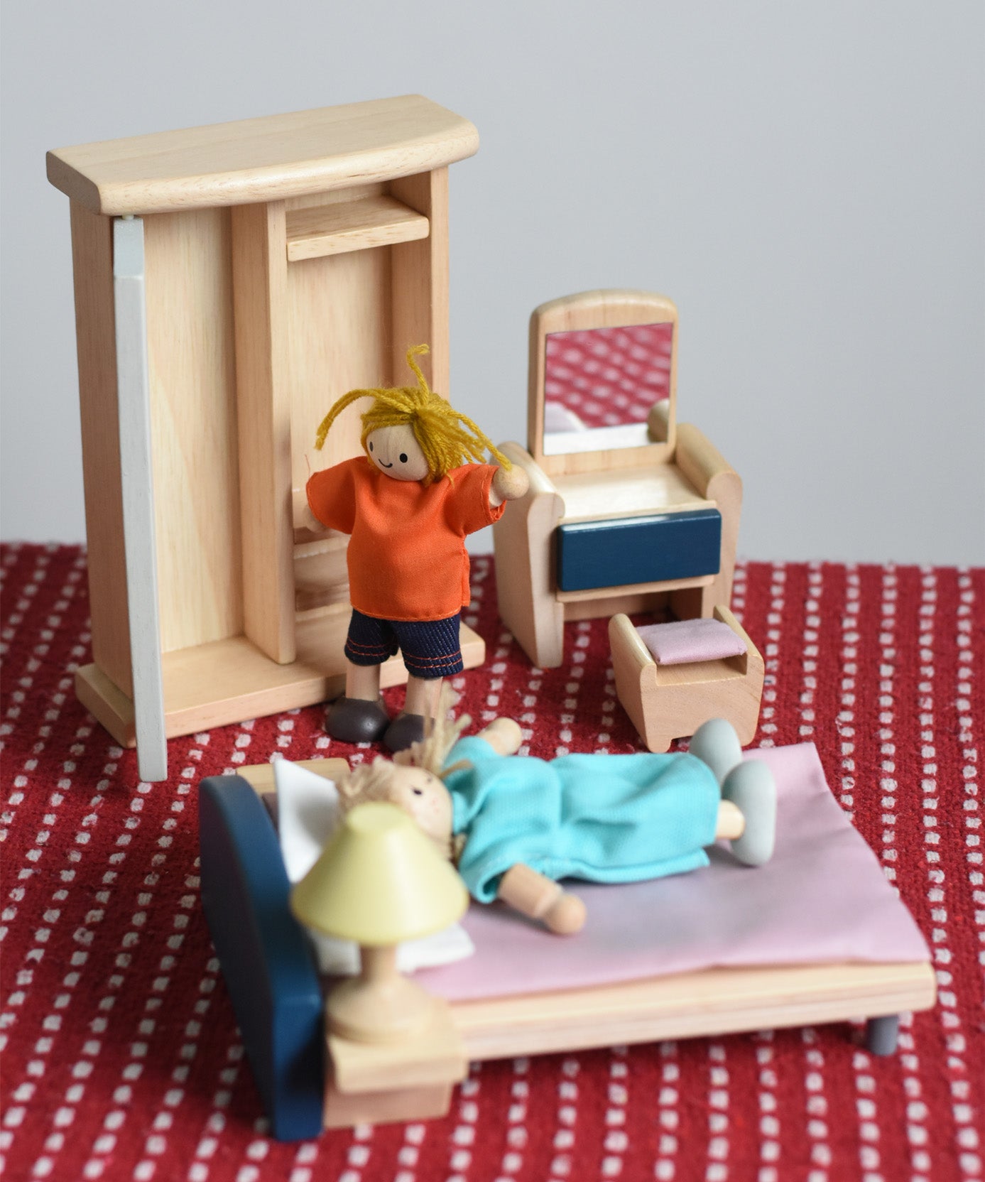 Two PlanToys peg dolls positioned in an imaginative play scene, with the orchard dollhouse wooden bedroom furniture. 