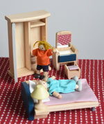 Two PlanToys peg dolls positioned in an imaginative play scene, with the orchard dollhouse wooden bedroom furniture. 