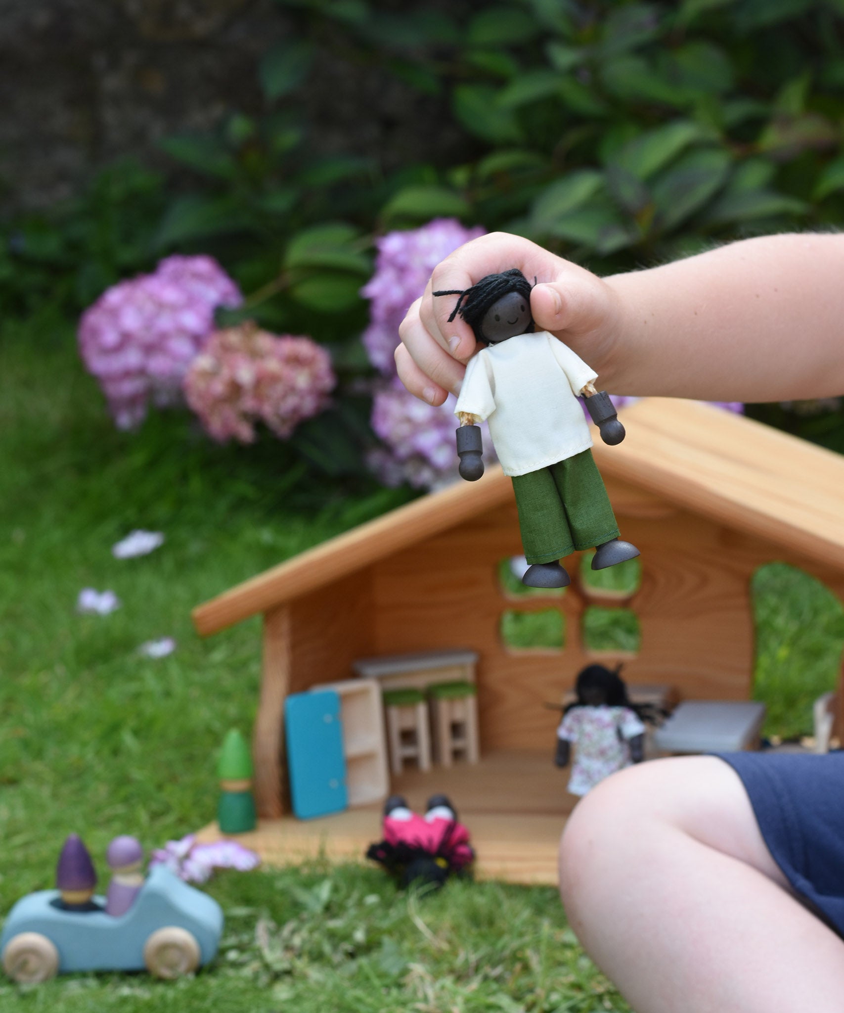 A child holding a doll from the PlanToys doll house family set in their hand.