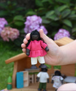 A child holding a doll from the PlanToys doll house family set in their hand.