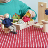 A child playing with the PlanToys Dolls House Family with White Skin, Blonde Hair. The child is placing the mum doll into the PlanToys wooden bath.
