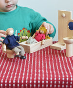 A child playing with the PlanToys Dolls House Family with White Skin, Blonde Hair. The child is placing the mum doll into the PlanToys wooden bath.