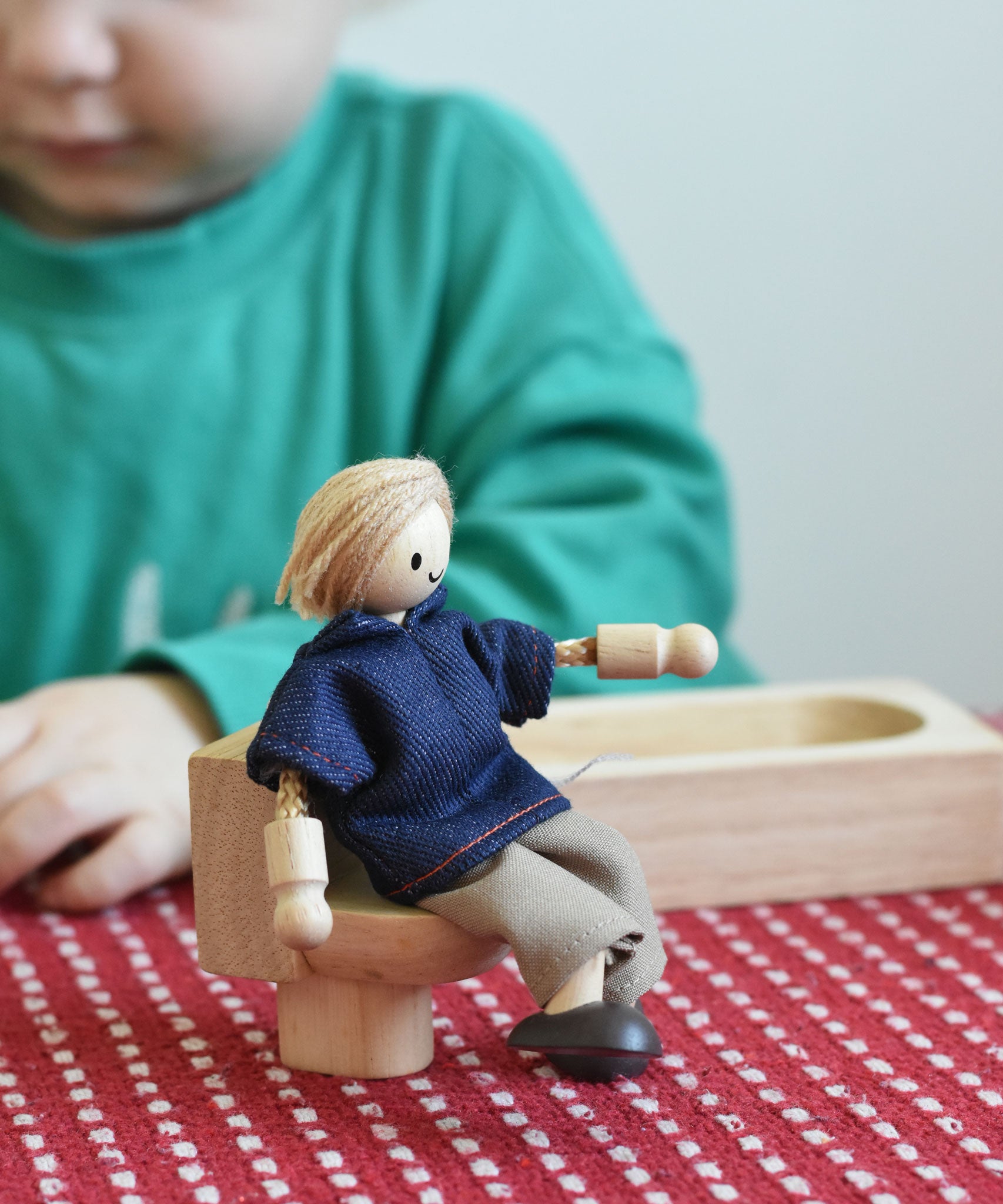 A dad doll from the PlanToys Dolls House Family with White Skin, Blonde Hair placed in a seated position on a little PlanToys wooden toilet. 