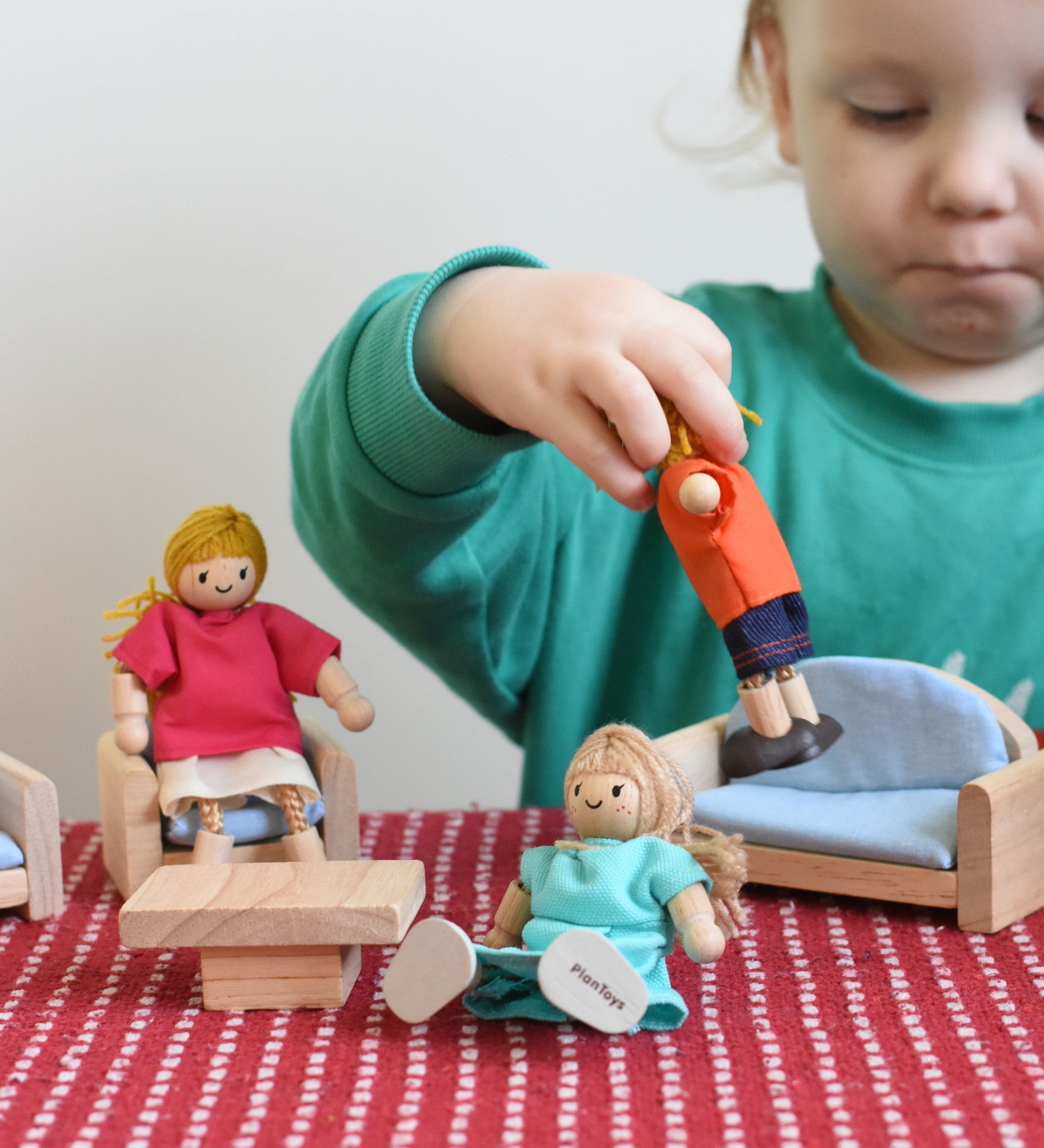 A child playing with the PlanToys Dolls House Family withWhite Skin, Blonde Hair and PlanToys dolls house furniture.