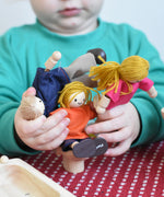 A child holding the PlanToys Dolls House Family with White Skin, Blonde Hair in their hands.