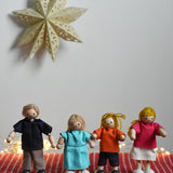 The PlanToys Dolls House Family with White Skin, Blonde Hair placed in a standing position and placed on a red blancket.