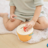 Child playing with the PlanToys drop and fit bucket wooden object permanence toy placing a red cylinder into the slot on the top of the bucket .