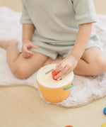 Child playing with the PlanToys drop and fit bucket wooden object permanence toy placing a red cylinder into the slot on the top of the bucket .