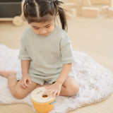 Child playing with the PlanToys drop and fit bucket wooden object permanence toy placing a red cylinder into the slot on the top of the bucket .