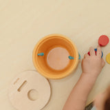 Overhead view of the PlanToys drop and fit bucket wooden object permanence toy with the lid lifted off.