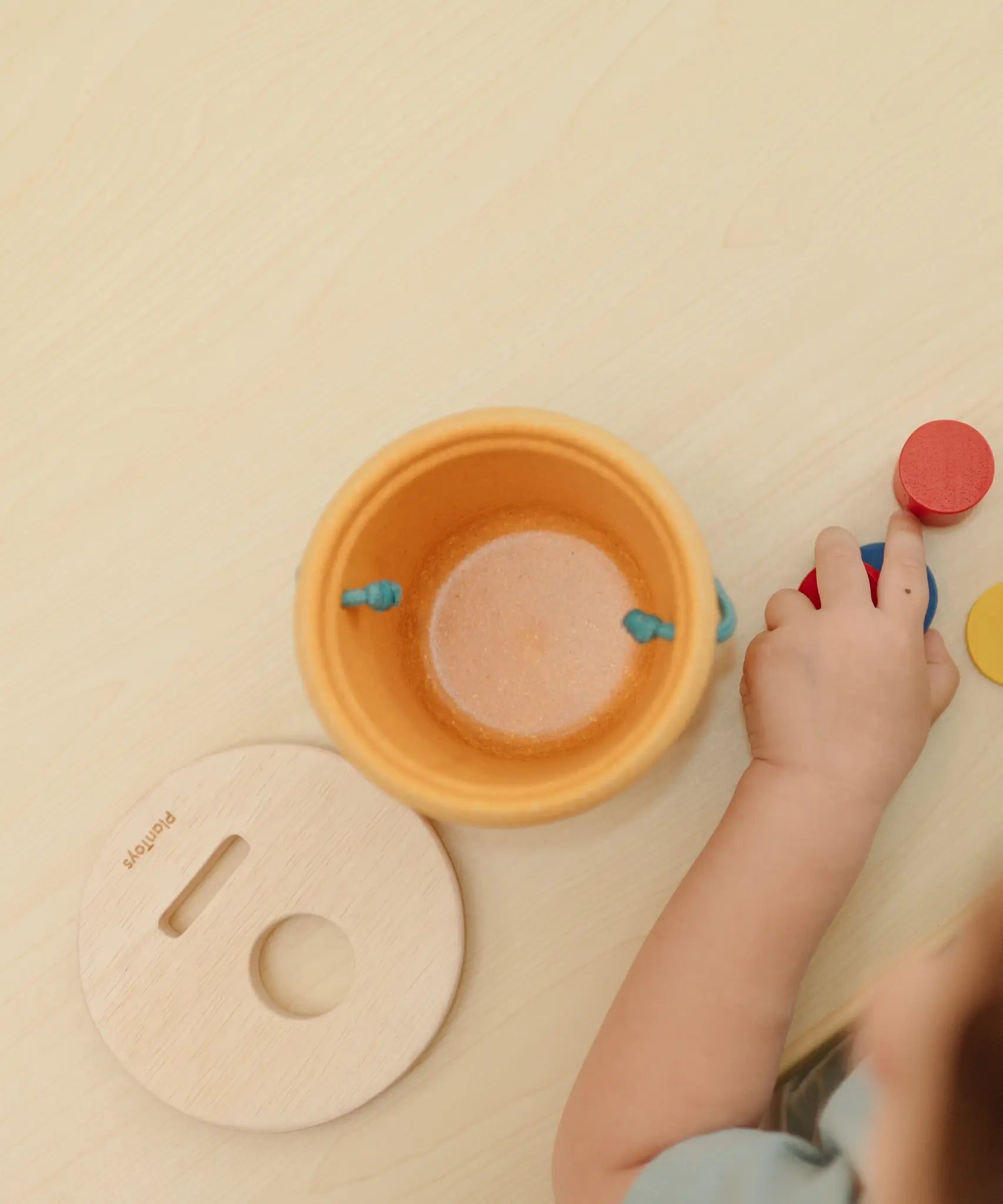 Overhead view of the PlanToys drop and fit bucket wooden object permanence toy with the lid lifted off.