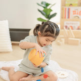 Child playing with the PlanToys drop and fit bucket wooden object permanence toy tipping the coins and cylinder out of the bucket.