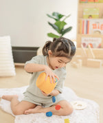 Child playing with the PlanToys drop and fit bucket wooden object permanence toy tipping the coins and cylinder out of the bucket.