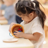 Child playing with the PlanToys drop and fit bucket wooden object permanence toy emptying the contents.