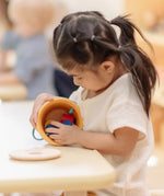Child playing with the PlanToys drop and fit bucket wooden object permanence toy emptying the contents.