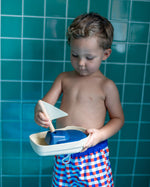 Close up of a young boy holding the PlanToys solid wooden sail boat toy in front of some blue tiles