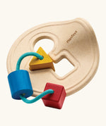PlanToys first shape sorter wooden baby toy. Wood frame with three shapes attached on string, blue cylinder, red cube and yellow triangle. 