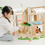 A child sitting besides the PlanToys Green Dolls' House and Furniture Set. The child is reaching for one of the pieces.