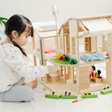 A child sitting besides the PlanToys Green Dolls' House and Furniture Set. The child is reaching for one of the pieces.