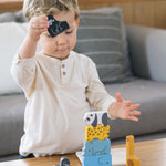 A child stacking the pieces from the Plan Toys Animal Puzzle Game
on a coffee table, he has the black gorilla figure in his hand ready to stack.