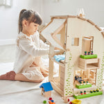 A child sitting besides the PlanToys Green Dolls' House and Furniture Set. 