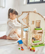 A child sitting besides the PlanToys Green Dolls' House and Furniture Set. 
