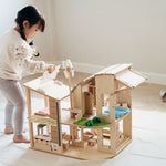 A child standing besides the PlanToys Green Dolls' House and Furniture Set. The child is holding the solar panel in their hand ready to place it back on the roof. 