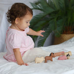A child sitting on a white duvet playing with the figures from the  PlanToys Farm Animals Set. 
