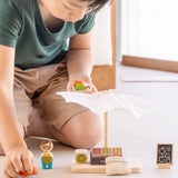 Child playing with the PlanToys Farmer's Market wooden toy playset, picking up wooden toy produce. 