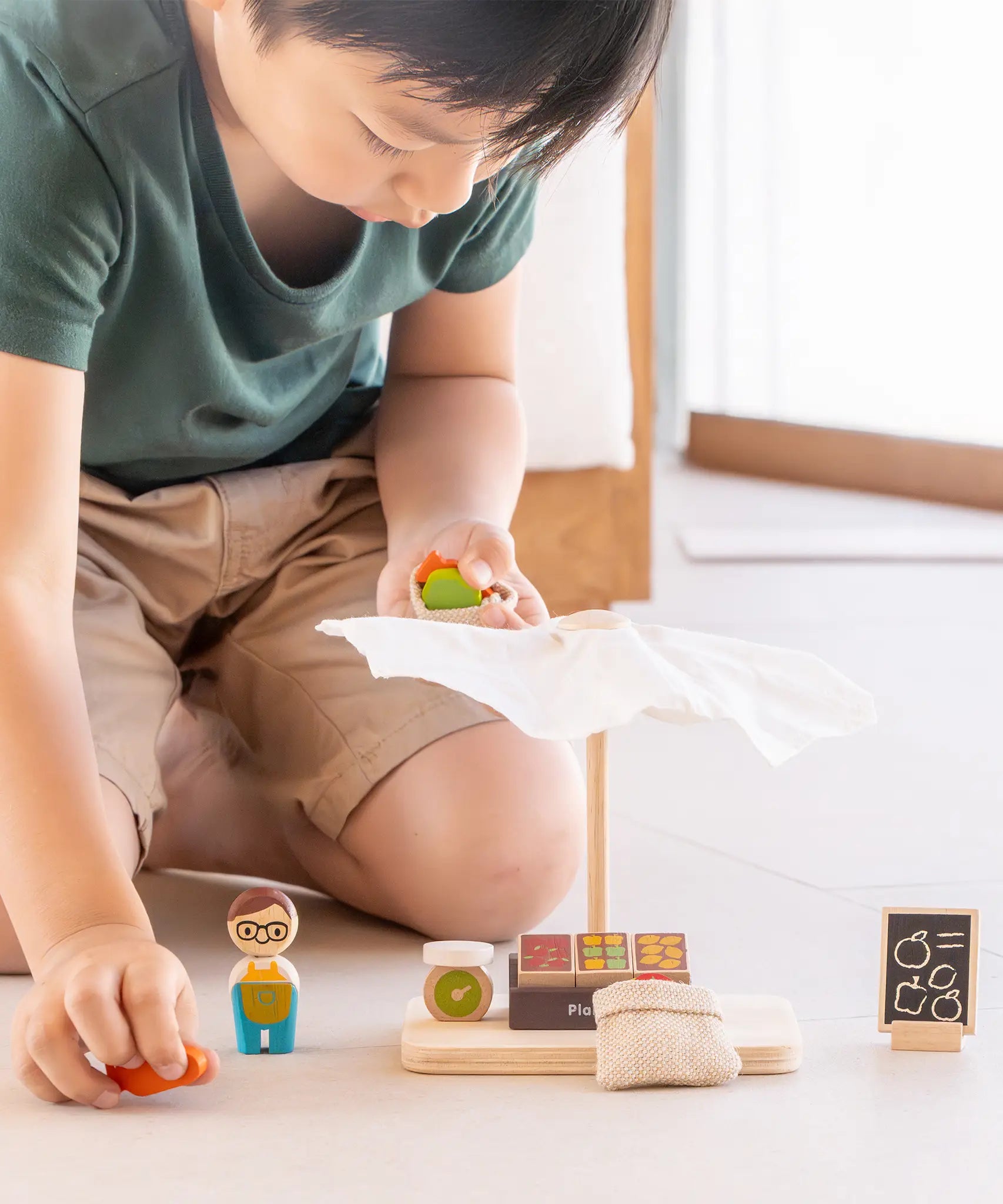 Child playing with the PlanToys Farmer's Market wooden toy playset, picking up wooden toy produce. 