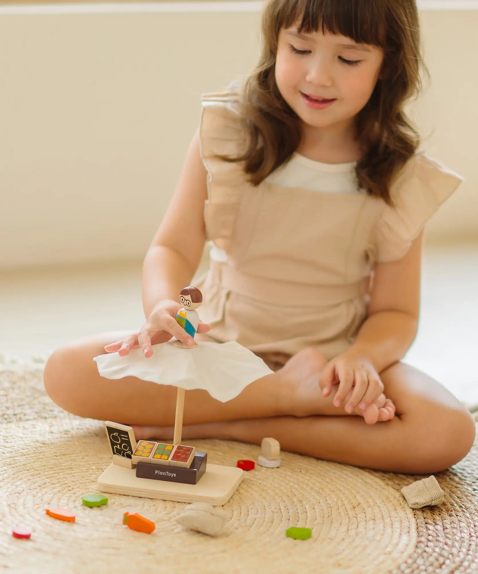 Child playing with the PlanToys Farmer's Market wooden toy playset. Child placing the worker wooden figure on the market stall canopy.