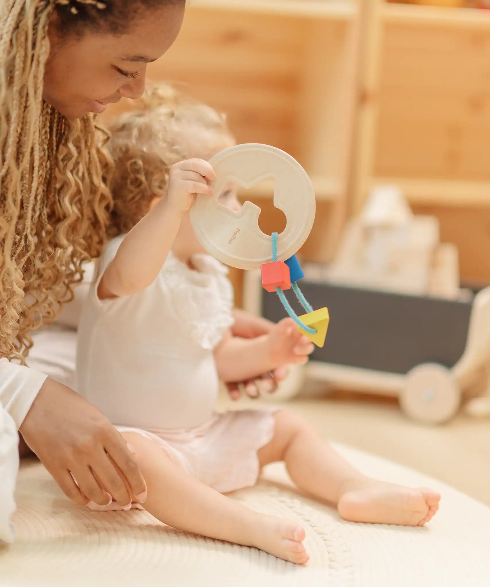 Child holding the PlanToys first shape sorter wooden baby toy with the wooden shapes hanging on the attached rope.
