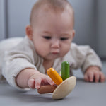A baby lying on their front playing with the PlanToys flexi jellyfish wooden toy. 