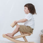 A child is rocking on the PlanToys Foldable Rocking Horse, their feet are placed on the frame at the bottom.