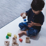 A child sitting on a floor playing with the PlanToys Geo Matching Blocks. 